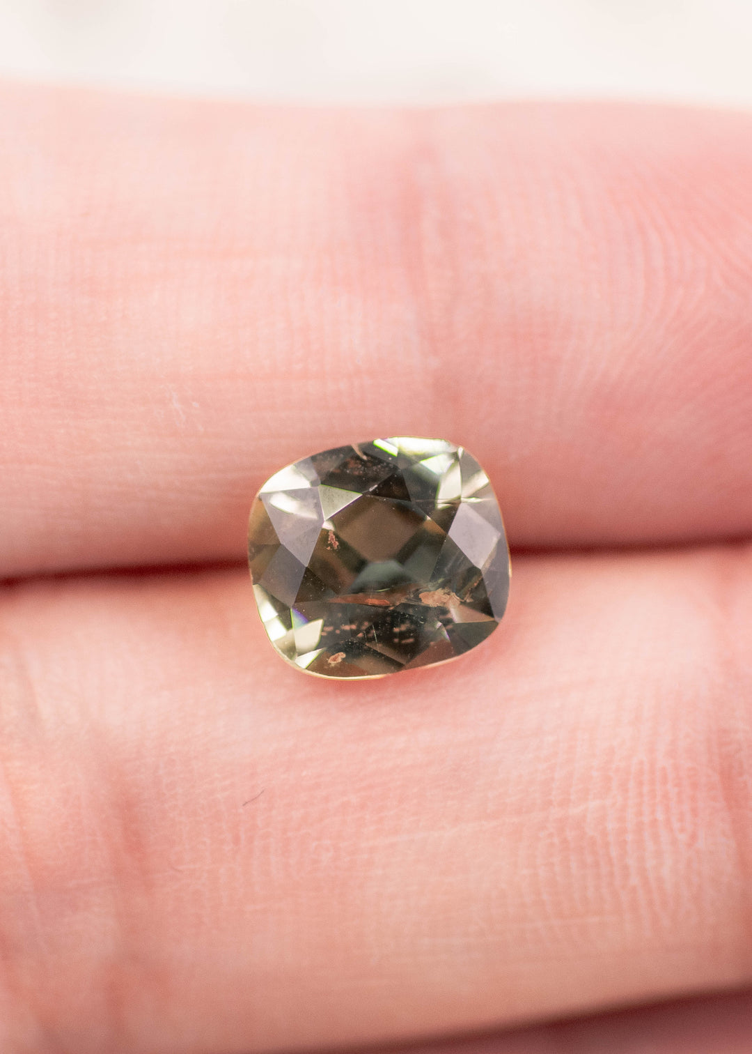 2.17 carat yellow green Tanzanite cushion cut resting on fingertip for scale, showing size, brilliance, and natural untreated color from Tanzania