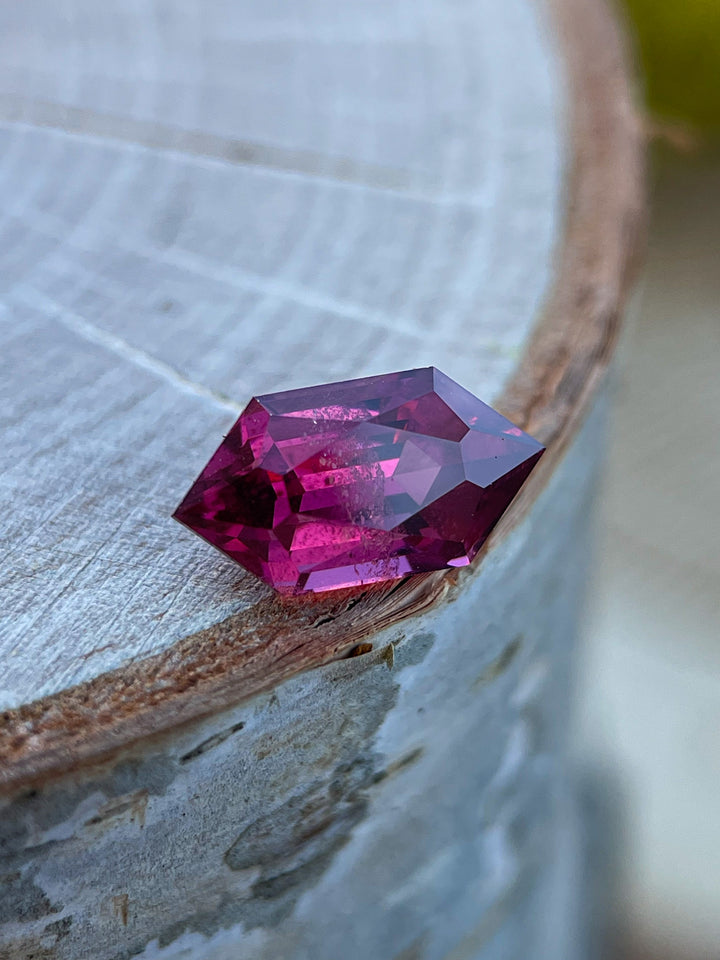 Close-up of a 2.40 carat garnet gemstone from Kenya with a custom geometric hexagon cut, featuring vibrant red and purple hues and natural untreated clarity.