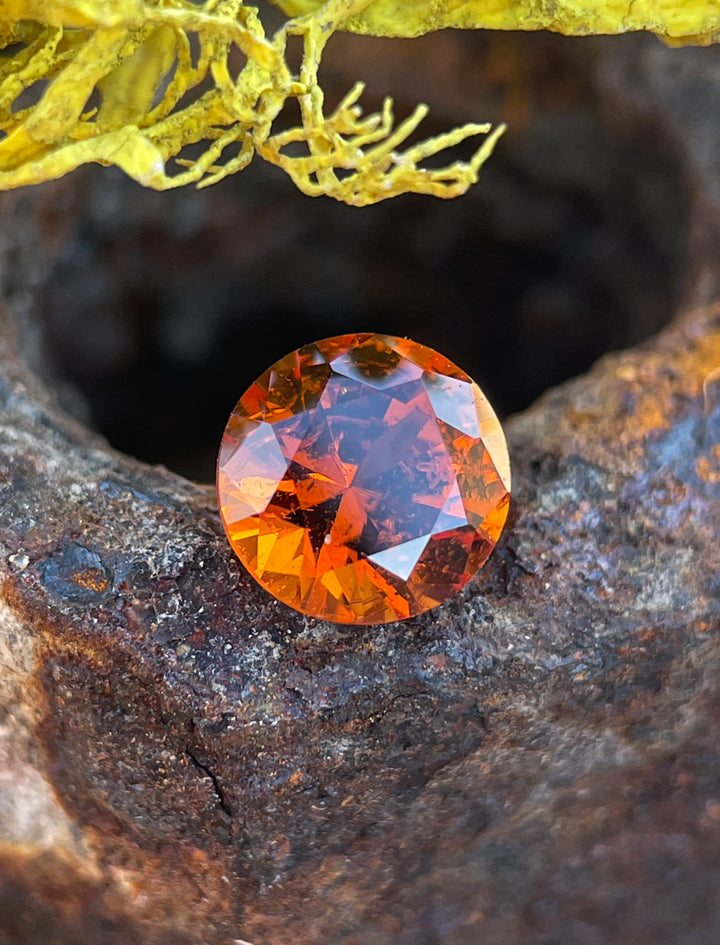 Close-up of a round brilliant cut Hessonite Garnet, 1.25 carats, in vivid orange-brown, captured in natural light.