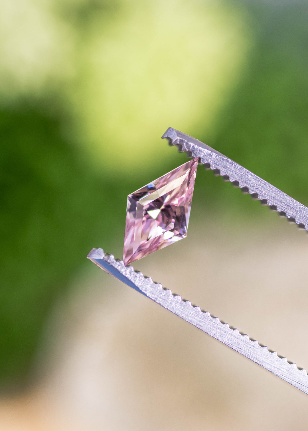 Loose salmon peach pink sapphire held in tweezers, highlighting the precision kite mix cut and natural pastel color from Madagascar.