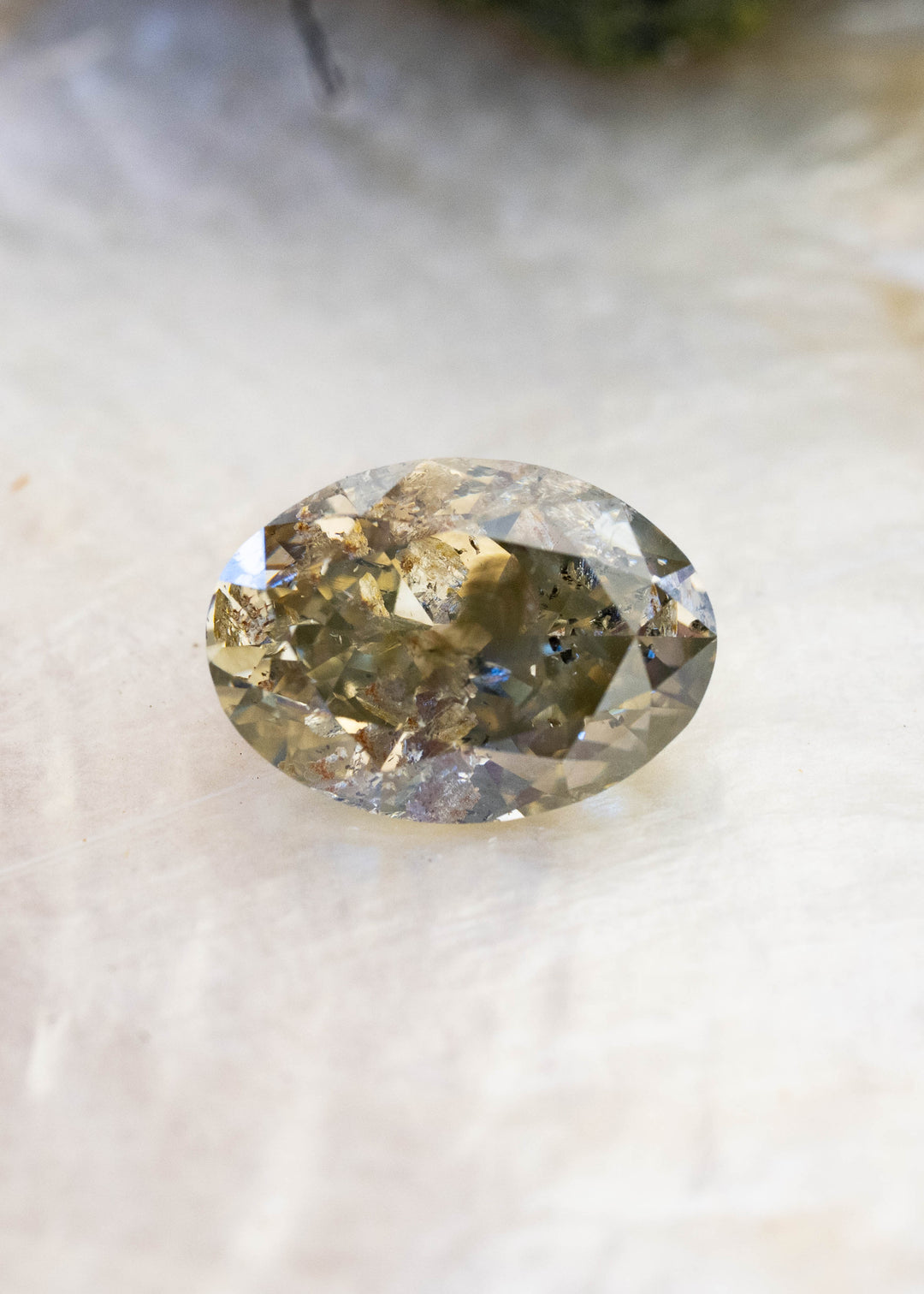 Close face-up view of a 1.88 carat antique oval brilliant cut natural diamond with greenish brown grey color and prominent salt and pepper inclusions throughout the stone.
