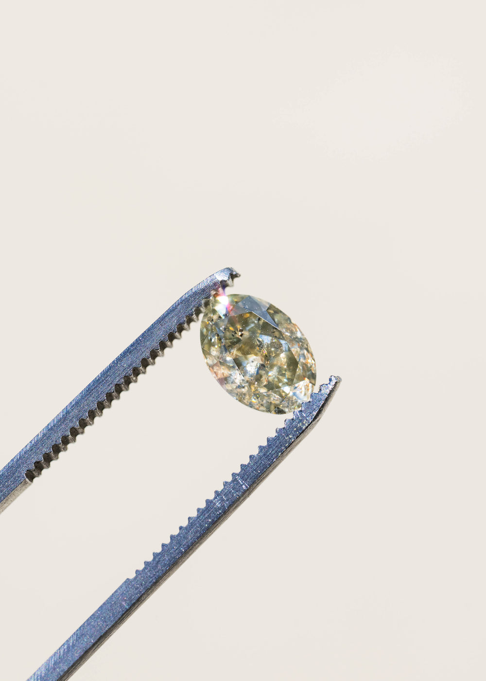 1.88 carat natural Zimbabwe diamond held in tweezers against a softly blurred background, displaying its antique oval shape, smoky green-brown color and distinctive salt and pepper inclusions.