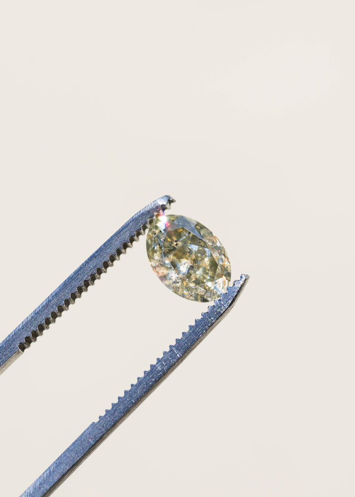 1.88 carat natural Zimbabwe diamond held in tweezers against a softly blurred background, displaying its antique oval shape, smoky green-brown color and distinctive salt and pepper inclusions.