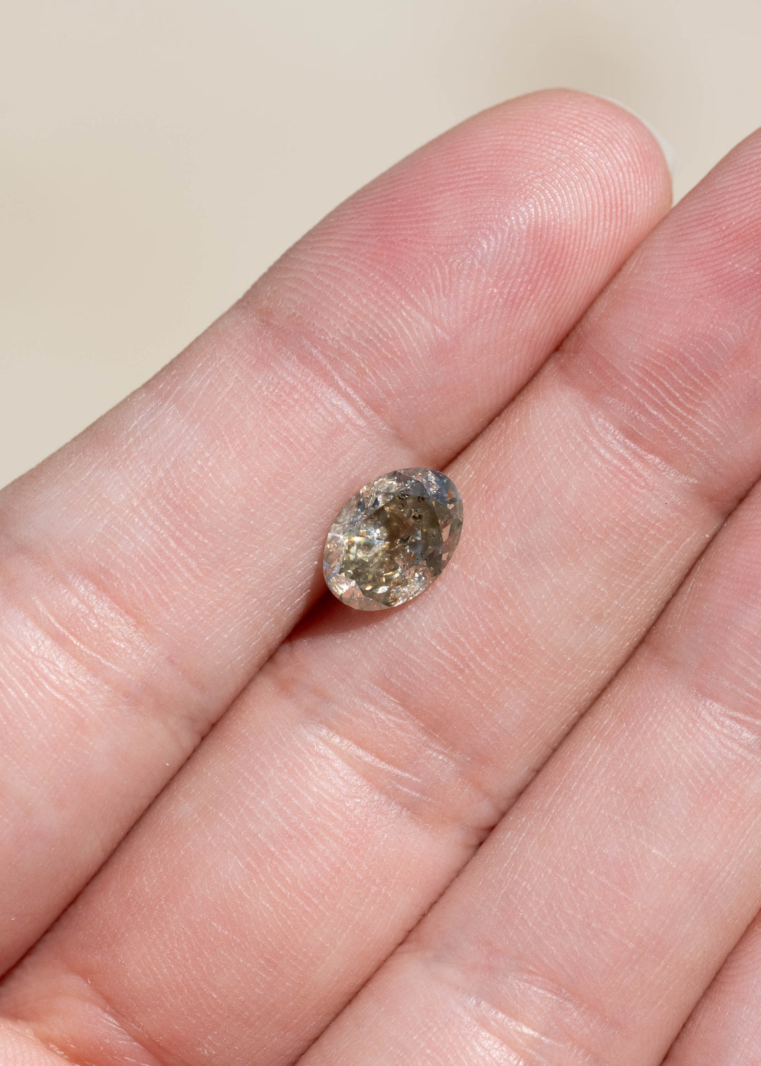 1.88 carat fancy greenish brown grey salt and pepper diamond resting on a hand, showing its elongated antique oval brilliant cut, earthy coloration and visible natural inclusions.