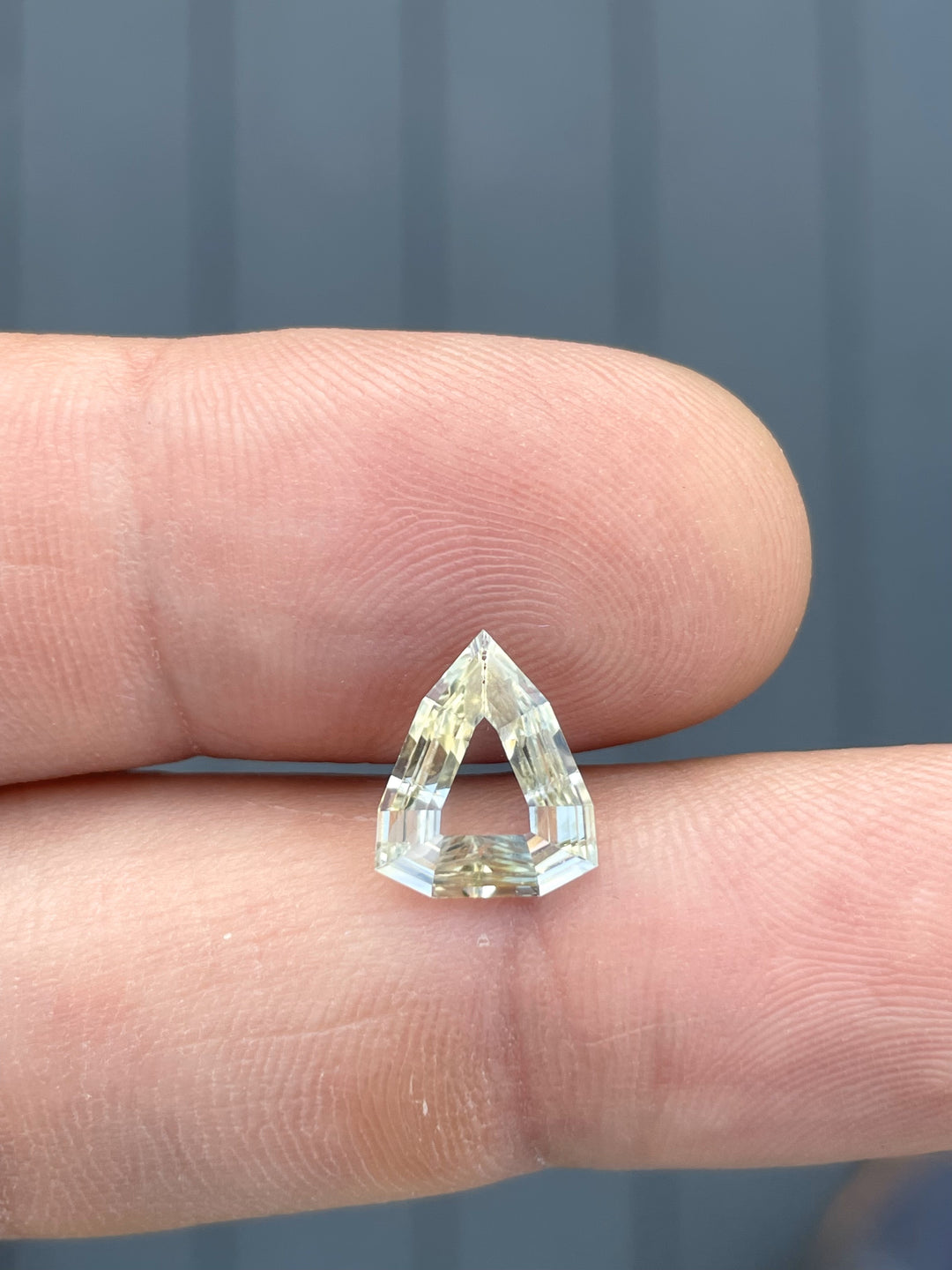 A 2.47-carat yellow-green sapphire displayed on a fingertip, emphasizing its modified geometric step cut and portrait shield shape. The stone’s precision cut and dimensions (11.68mm x 9.62mm x 2.63mm) make it stand out, untreated and sourced from Sri Lanka.