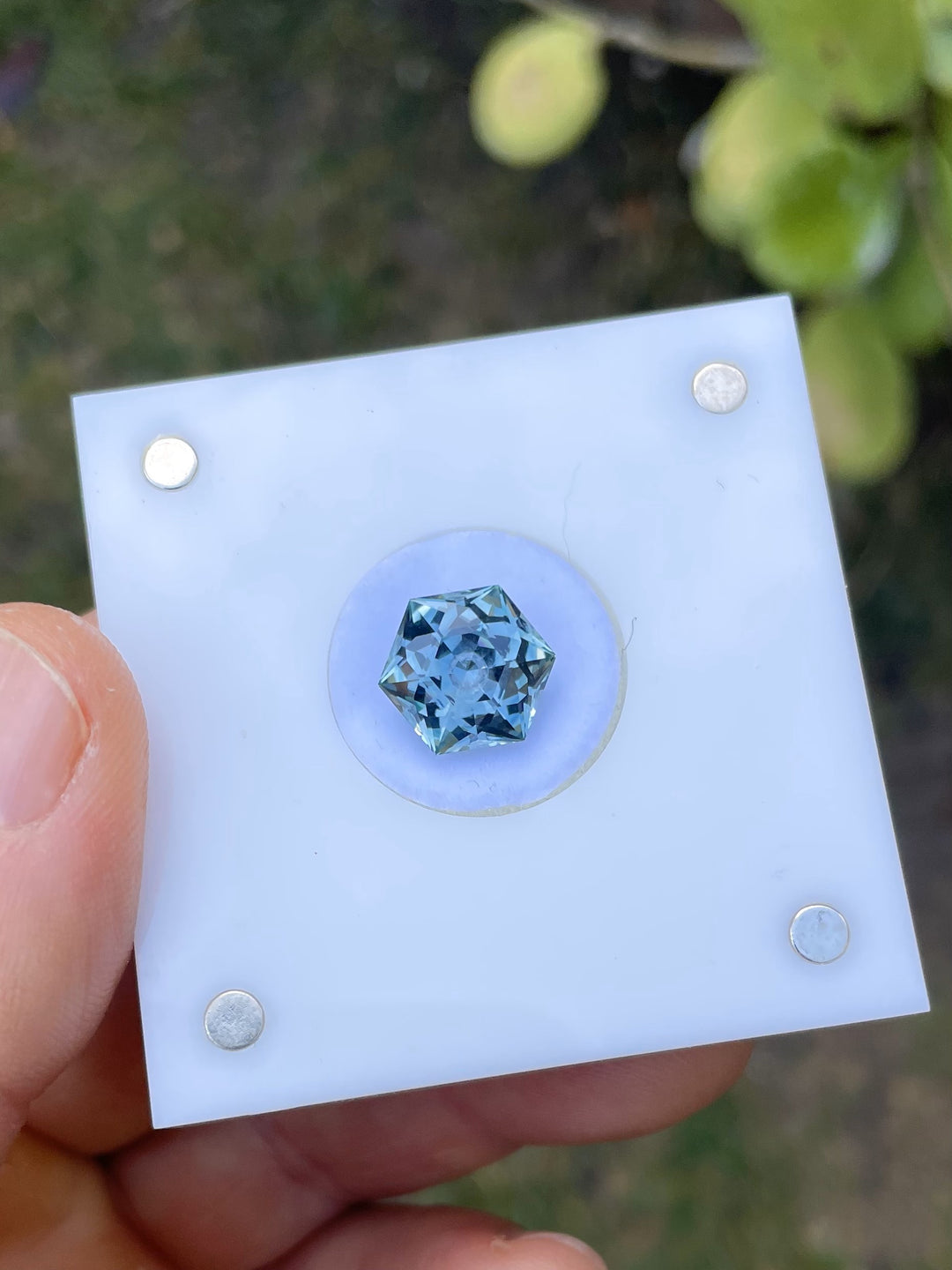 A 5.79-carat hexagonal modified brilliant cut sapphire mounted on a white display pad, offering a clear view of the gem's precision cut and the vivid interplay of blue and green colors.