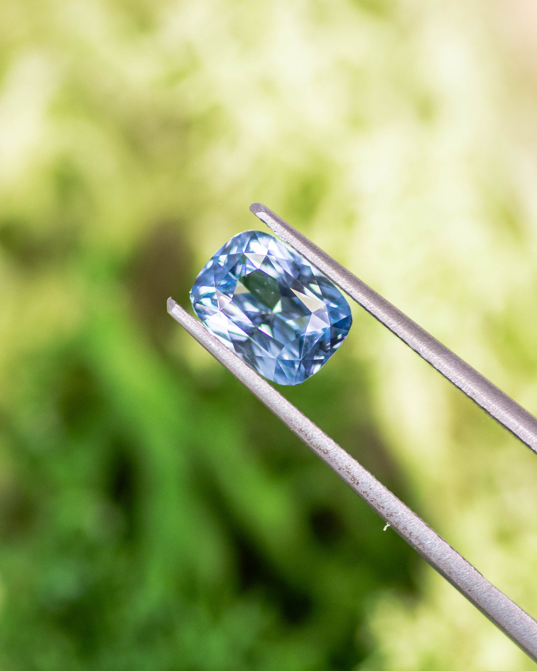 Seafoam and blue 2.04 carat heated sapphire displayed in tweezers outdoors, showing precision elongated cushion mixed cut and vibrant color zoning from Sakaraha, Madagascar.