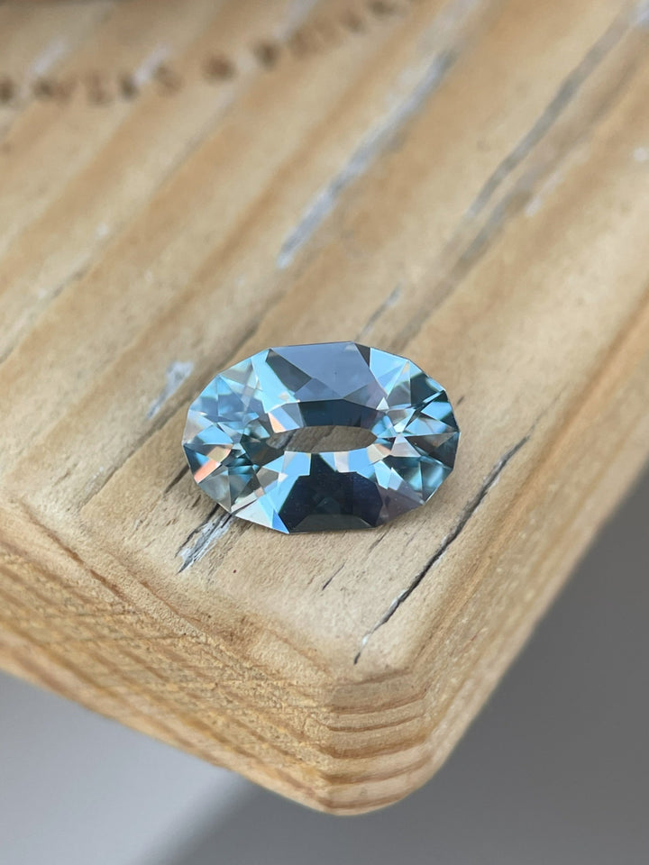 Stunning 1.61-carat seafoam blue sapphire in an oval brilliant cut, ethically sourced from Sri Lanka, placed on a wooden display.