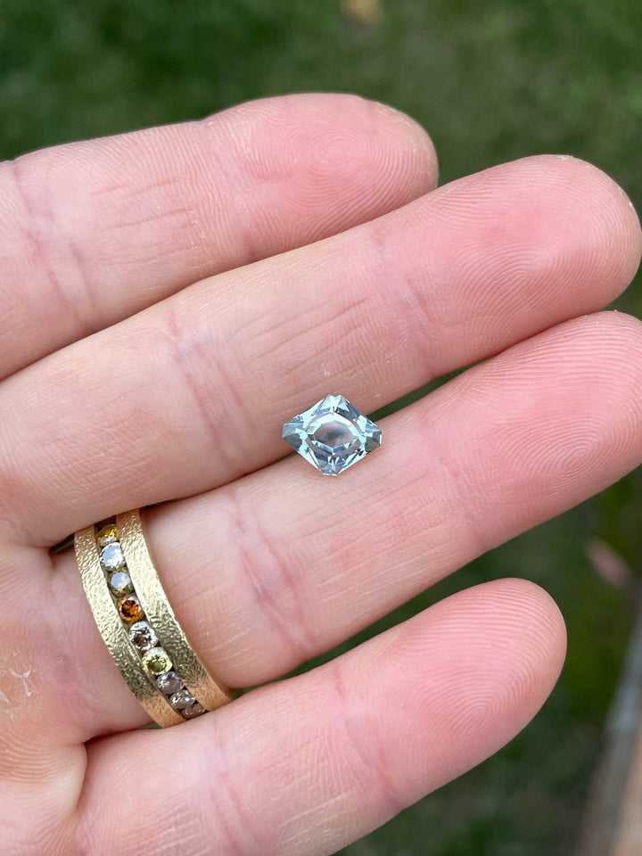 2.24 carat seafoam teal Sapphire displayed on fingertips, highlighting its geometric rhombus antique cut and pastel teal hues in natural light.