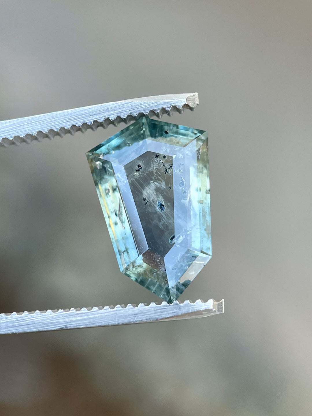 Close-up of a 5.48-carat sapphire in tweezers with a precision shield cut, revealing vivid teal and blue tones with natural inclusions.