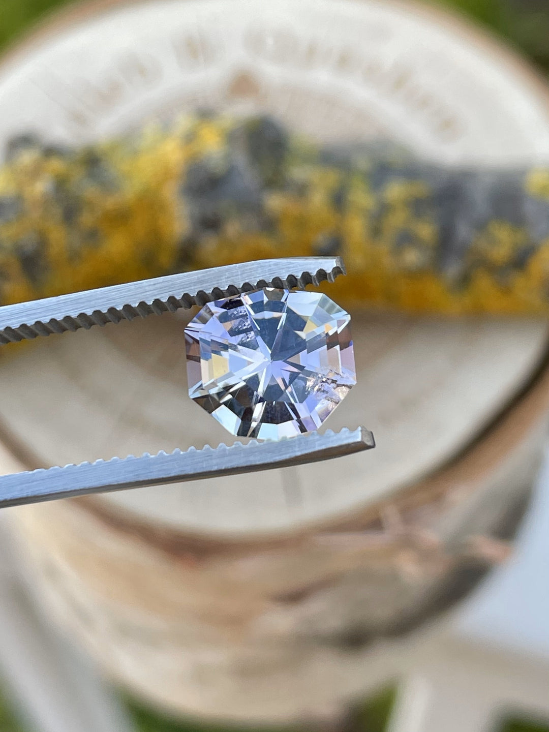 Close-up of a 3.33-carat Tanzanite in shield step cut held in gem tweezers, with a soft play of gray, pink, lavender, and teal hues, unheated and ethically sourced