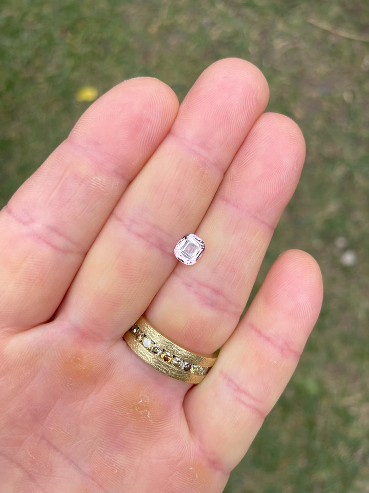 Hand holding a 1.19-carat cushion-cut pastel yellow sapphire, exhibiting a delicate peach tone. This ethically sourced gemstone originates from Sri Lanka and has not undergone any treatment.