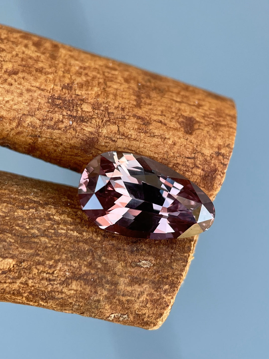 A close-up of a 3.09-carat color-change sapphire, shifting between pink and brown, resting on a natural wooden surface, highlighting its exquisite pear brilliant cut.