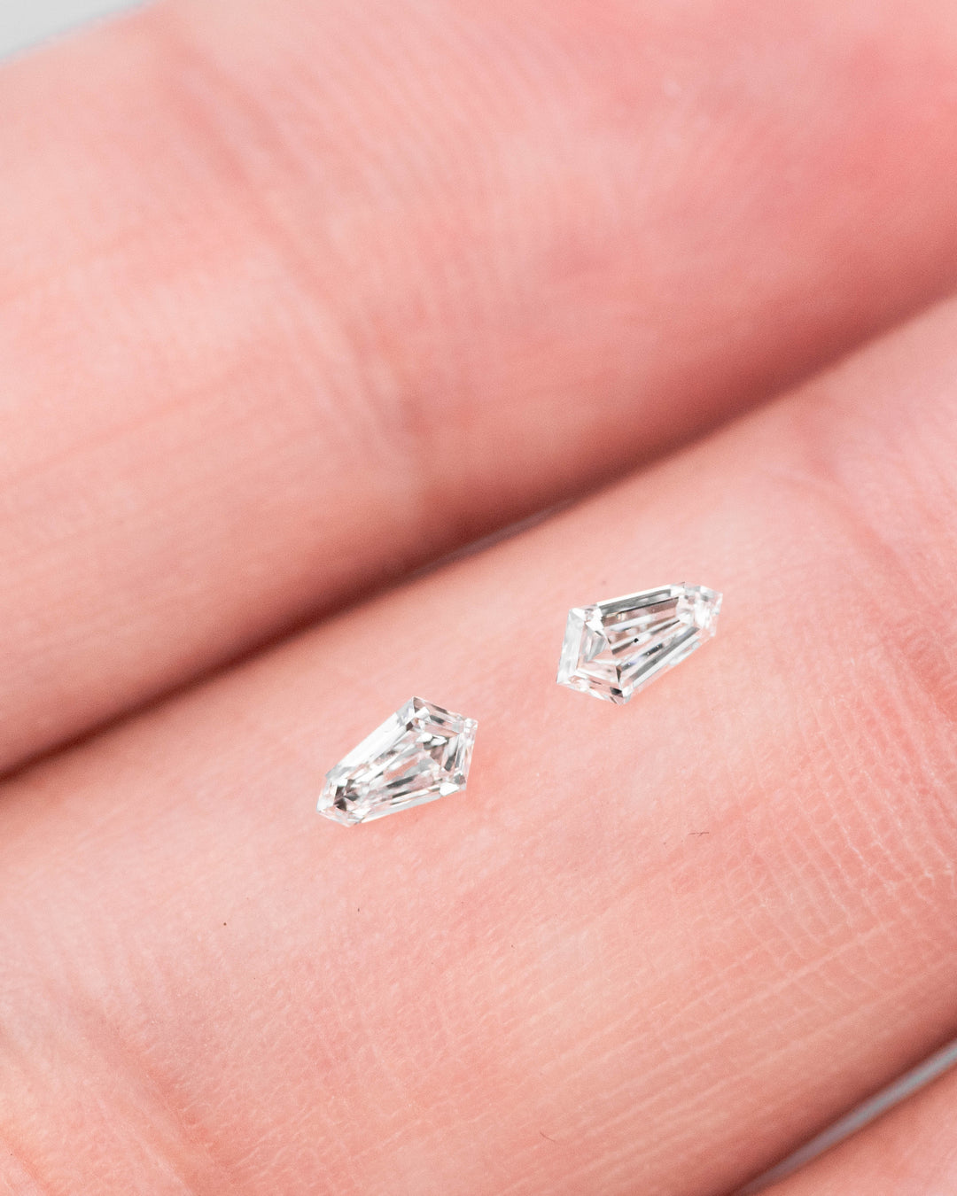 Pair of 0.18-carat D–E VVS clarity kite step cut diamonds resting on a fingertip, highlighting matched dimensions, sparkle, and precision cutting, ethically sourced from South Africa.