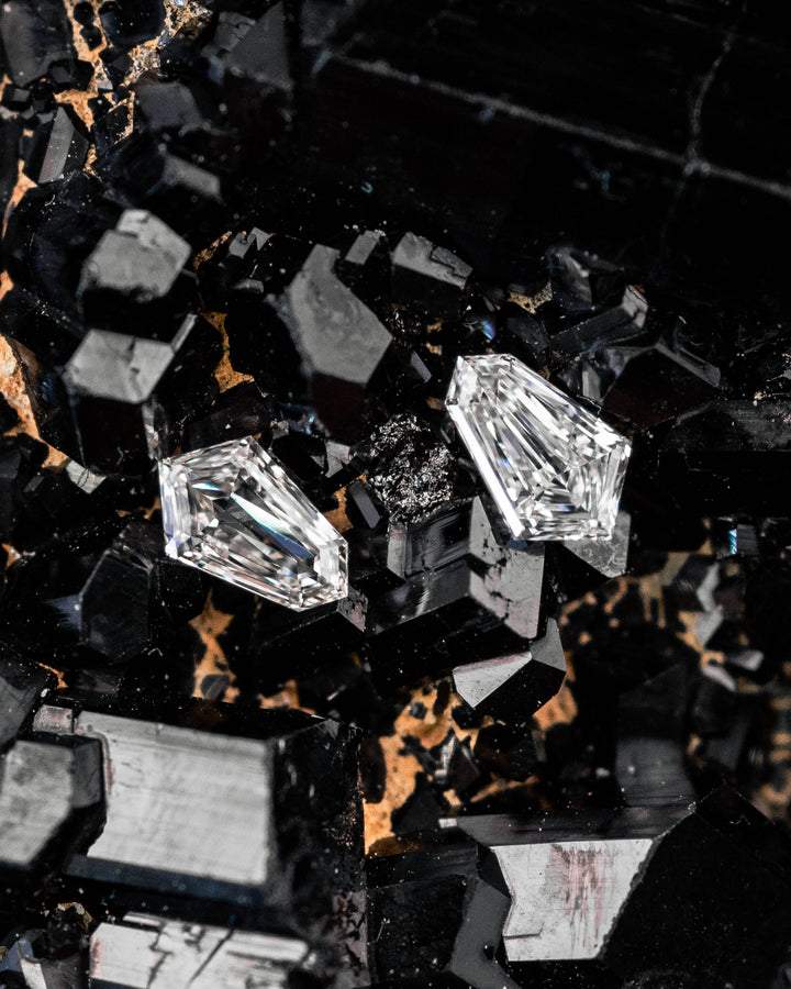 Matched pair of 0.19 carat F-G color VVS-VS clarity kite step cut diamonds displayed on a black crystal mineral matrix, showcasing the geometric faceting and sparkle of the precision-cut stones.
