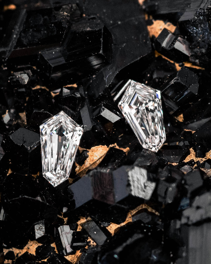 0.19-carat D-E color VVS clarity kite step-cut diamond pair displayed on black crystal mineral surface, highlighting precision geometric faceting, clean clarity, and bright reflections — loose South African diamonds for luxury jewelry.
