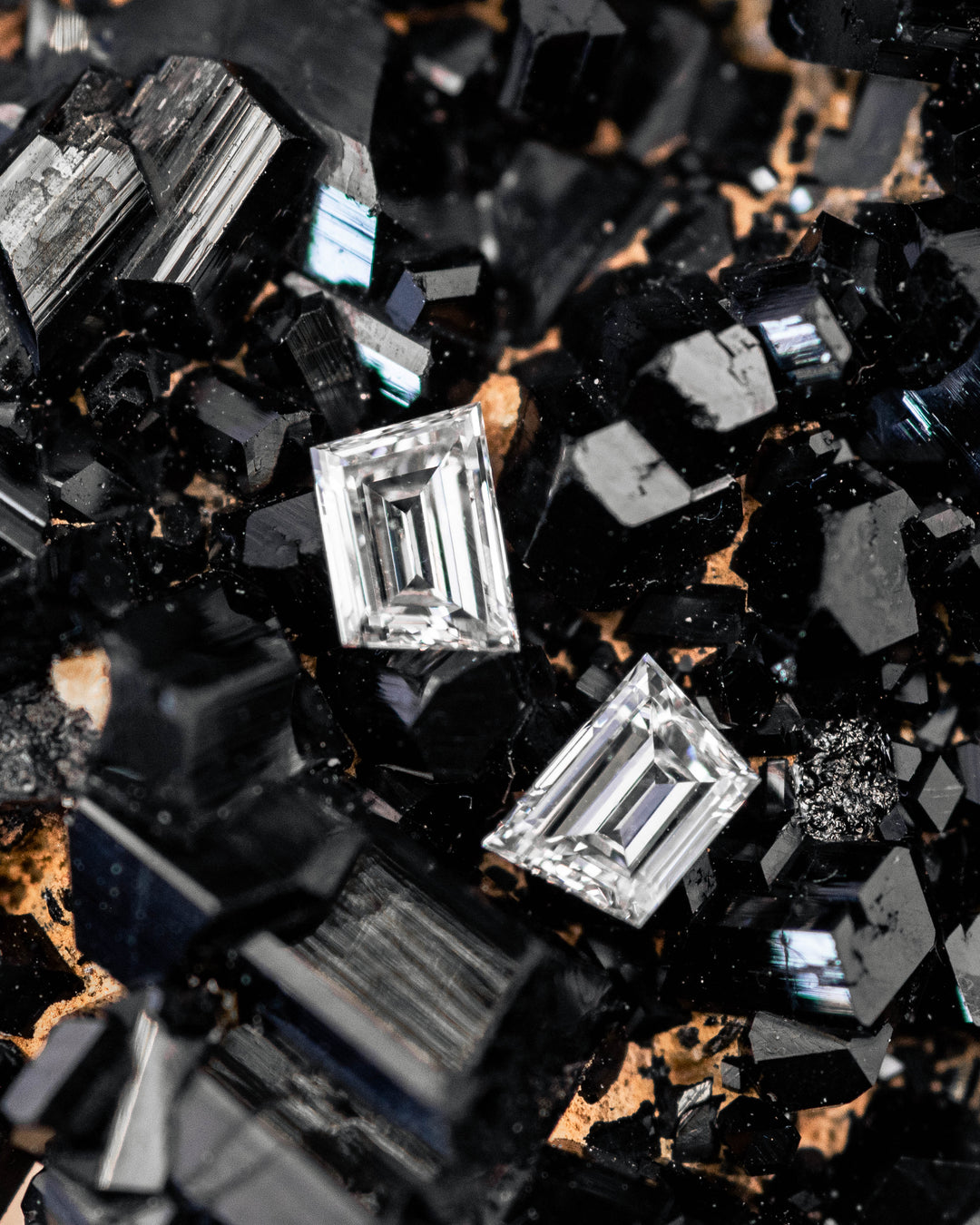 0.32 carat F color VVS clarity trapezoid step cut diamond pair from South Africa resting on a black crystal mineral matrix, highlighting the geometric step-cut facets, natural sparkle, and untreated diamond surfaces.