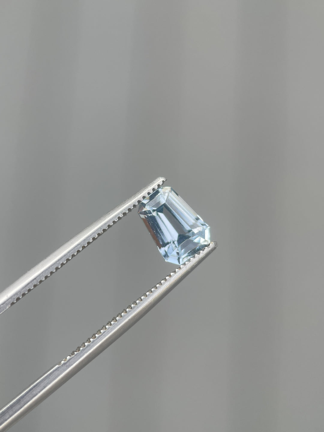 1.64 carat pale blue sapphire held by tweezers, revealing the intricate fancy mixed cut and clear, icy-blue hue. This gem, originating from Sri Lanka, highlights exceptional craftsmanship and natural beauty.
