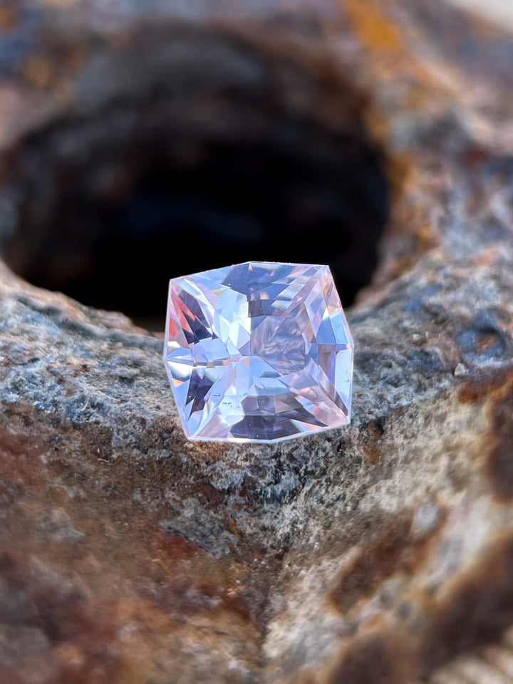 A 1.04-carat pink peach sapphire with a fancy mixed cushion cut, set against a textured rock background to highlight its natural brilliance and untreated origin.