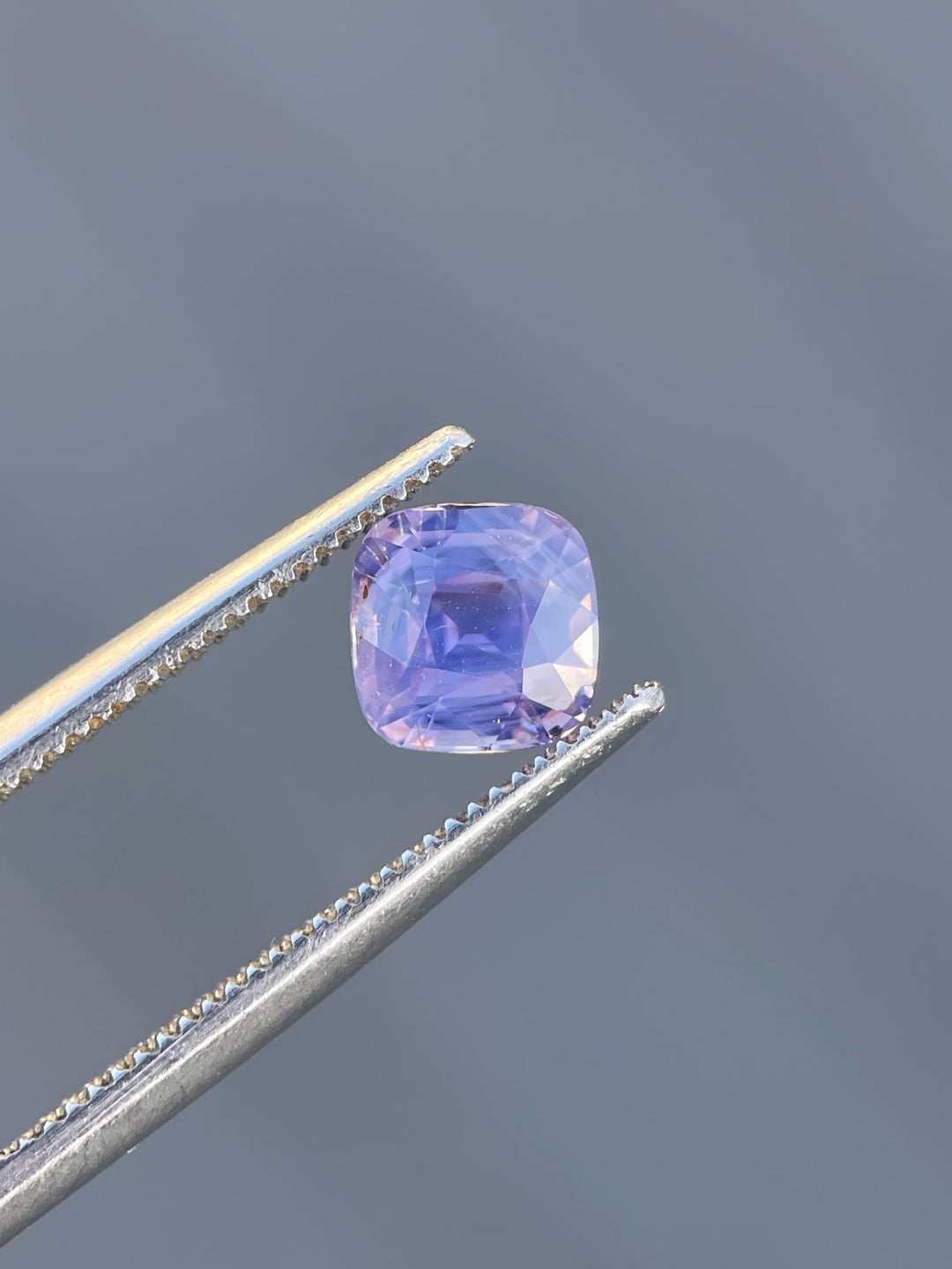 Detailed view of a Sri Lankan sapphire gemstone, weighing 1.53 carats, in a cushion cut with opalescent pink to purple tones and untreated clarity.