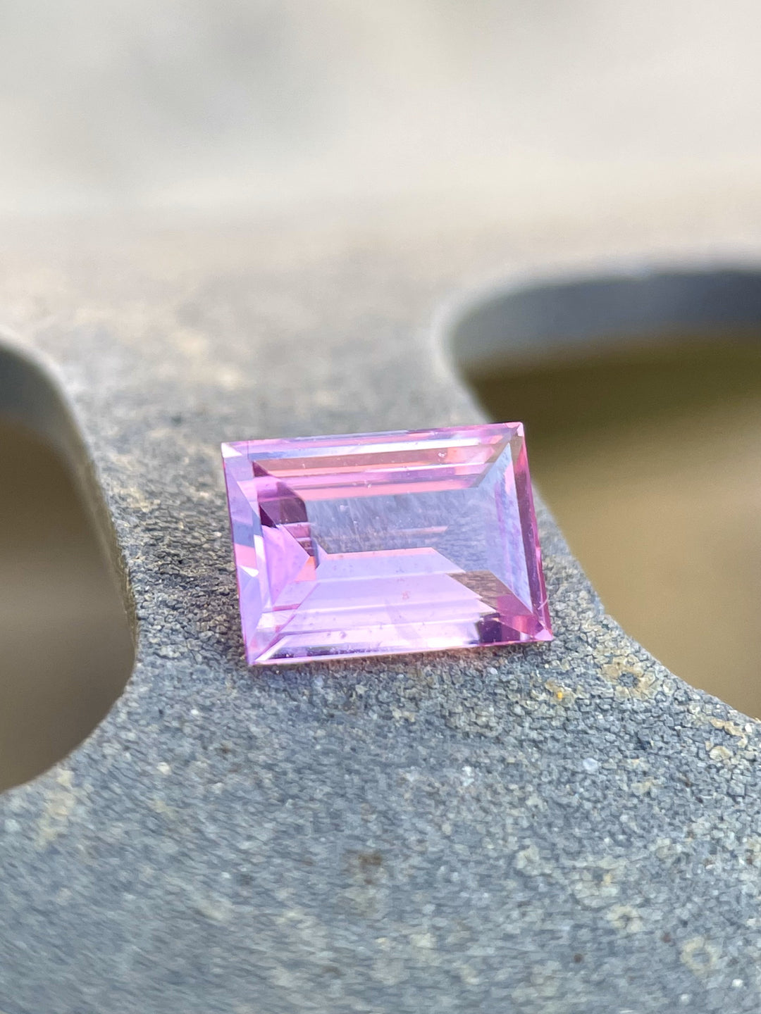 Elegant 1.10 carat pink, purple, and mulberry sapphire, displayed in its emerald cut on a soft, textured surface, highlighting its pristine clarity and natural origin from Sri Lanka.