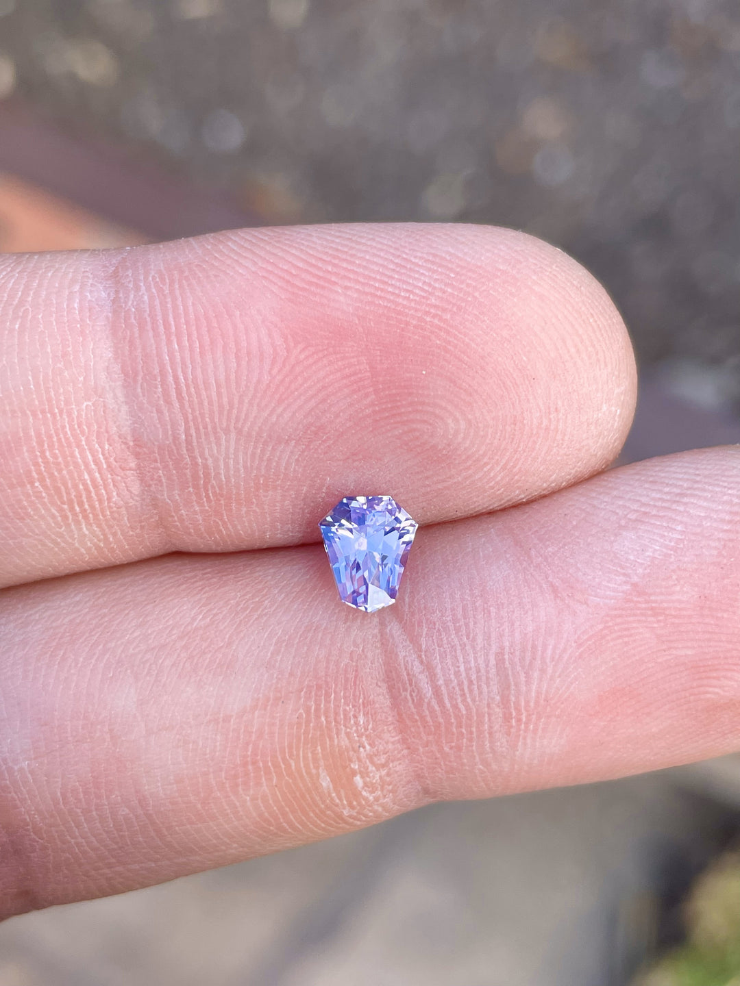 Exquisite 1.14 carat custom shield cut sapphire resting on a hand, showcasing vivid pink, lavender, and blue hues, measured at 6.75 x 5.70 x 4.20 mm from Sri Lanka, untreated.
