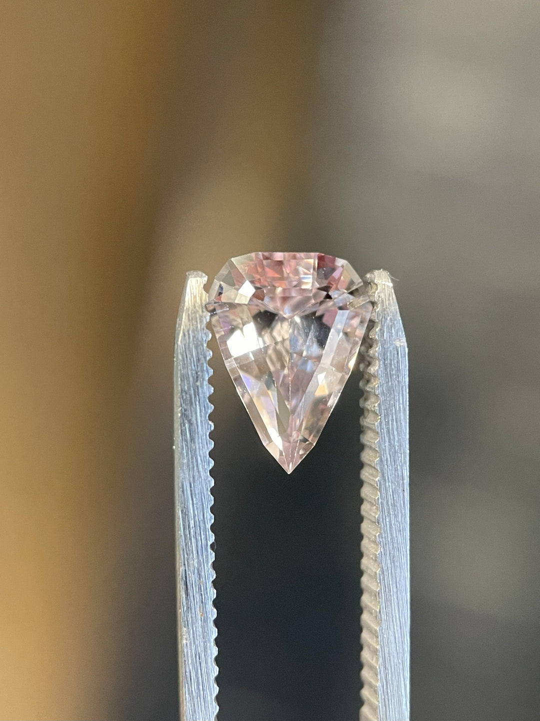 A vibrant color-changing sapphire resting on an elegant display, transitioning from pink to peach hues. The gemstone weighs 2.09 carats and is expertly cut in a modified geometric step cut shield.