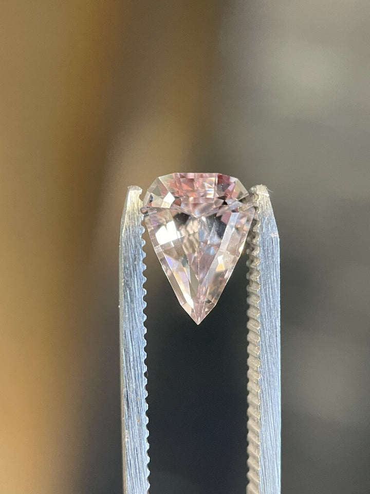 A vibrant color-changing sapphire resting on an elegant display, transitioning from pink to peach hues. The gemstone weighs 2.09 carats and is expertly cut in a modified geometric step cut shield.