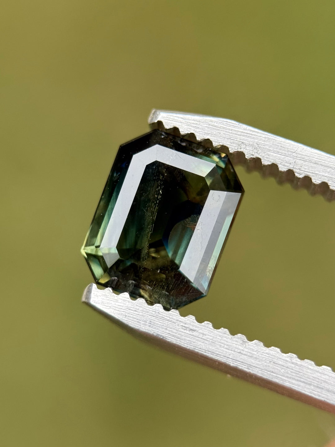 Close-up of a 2.14 carat parti sapphire in tweezers, showcasing emerald cut and teal-blue color zoning.