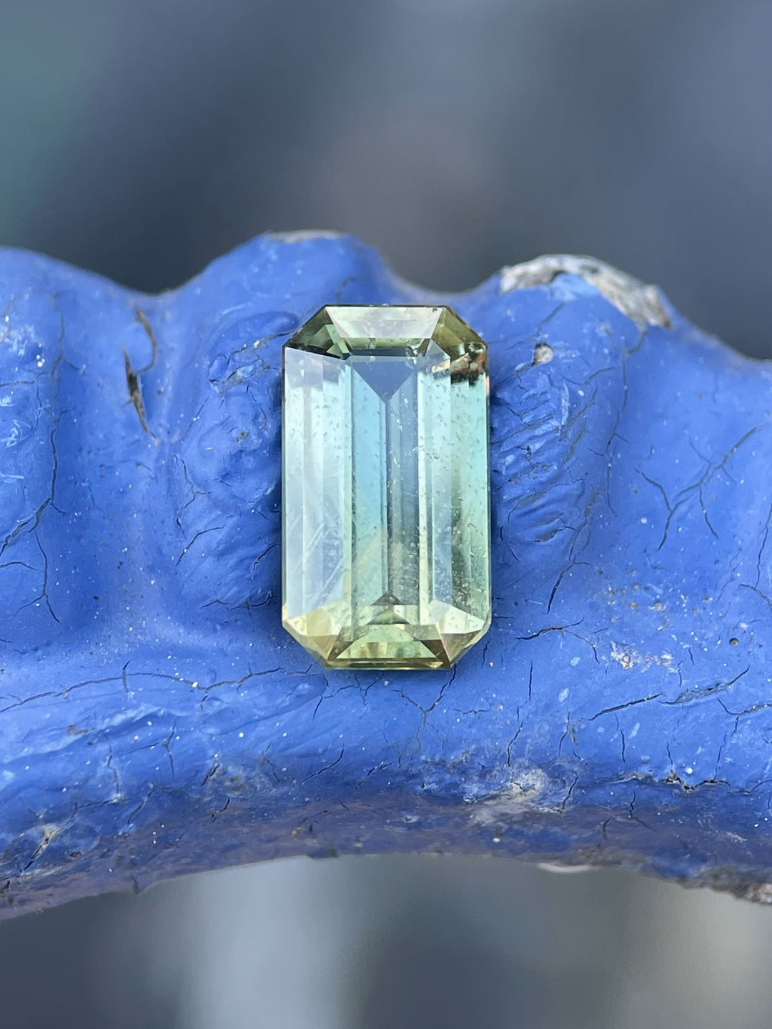 Close-up of a 2.24-carat sapphire resting on a textured blue surface, showcasing vivid yellow, teal, and green colors.