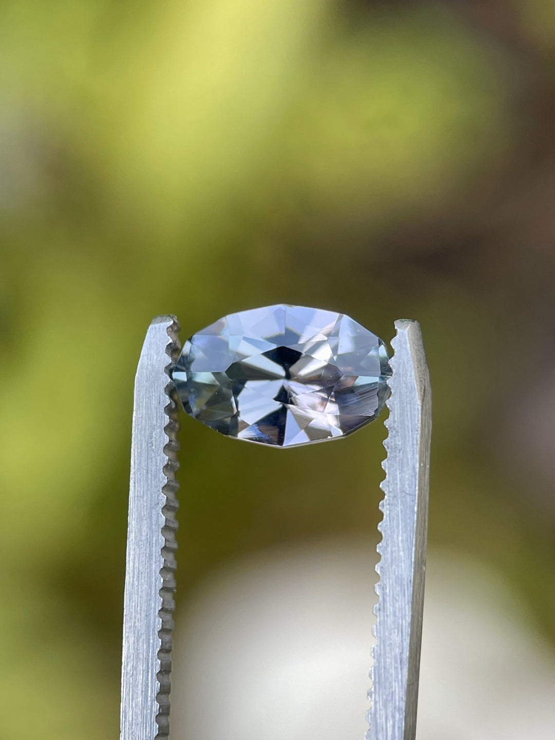 Close-up of 1.78-carat Tanzanite held in tweezers, displaying vibrant teal and mermaid hues in a custom geometric oval cut.