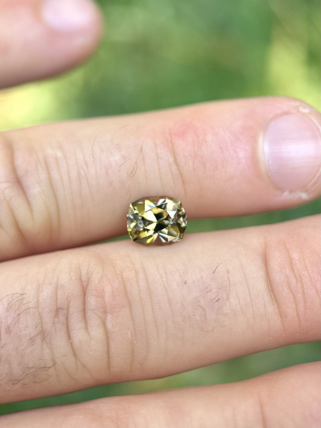 2.60-carat cushion-cut Tanzanite in golden yellow hue displayed on fingers – ethically sourced from Merelani Hills, Arusha, Tanzania