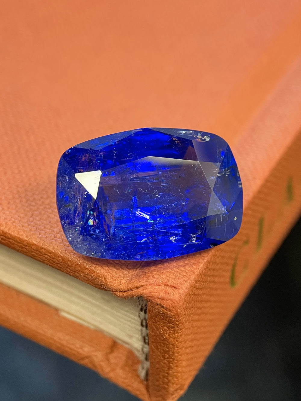 A 27.31-carat cushion-cut tanzanite placed on a vintage orange book, showcasing rich blue-violet hues and brilliant faceting.