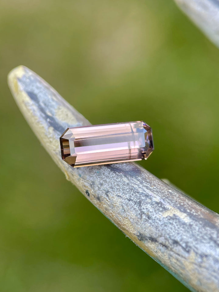 2.12ct elongated emerald cut Tanzanite with lavender, peach, and pink tones resting on a curved natural surface for a rustic look.