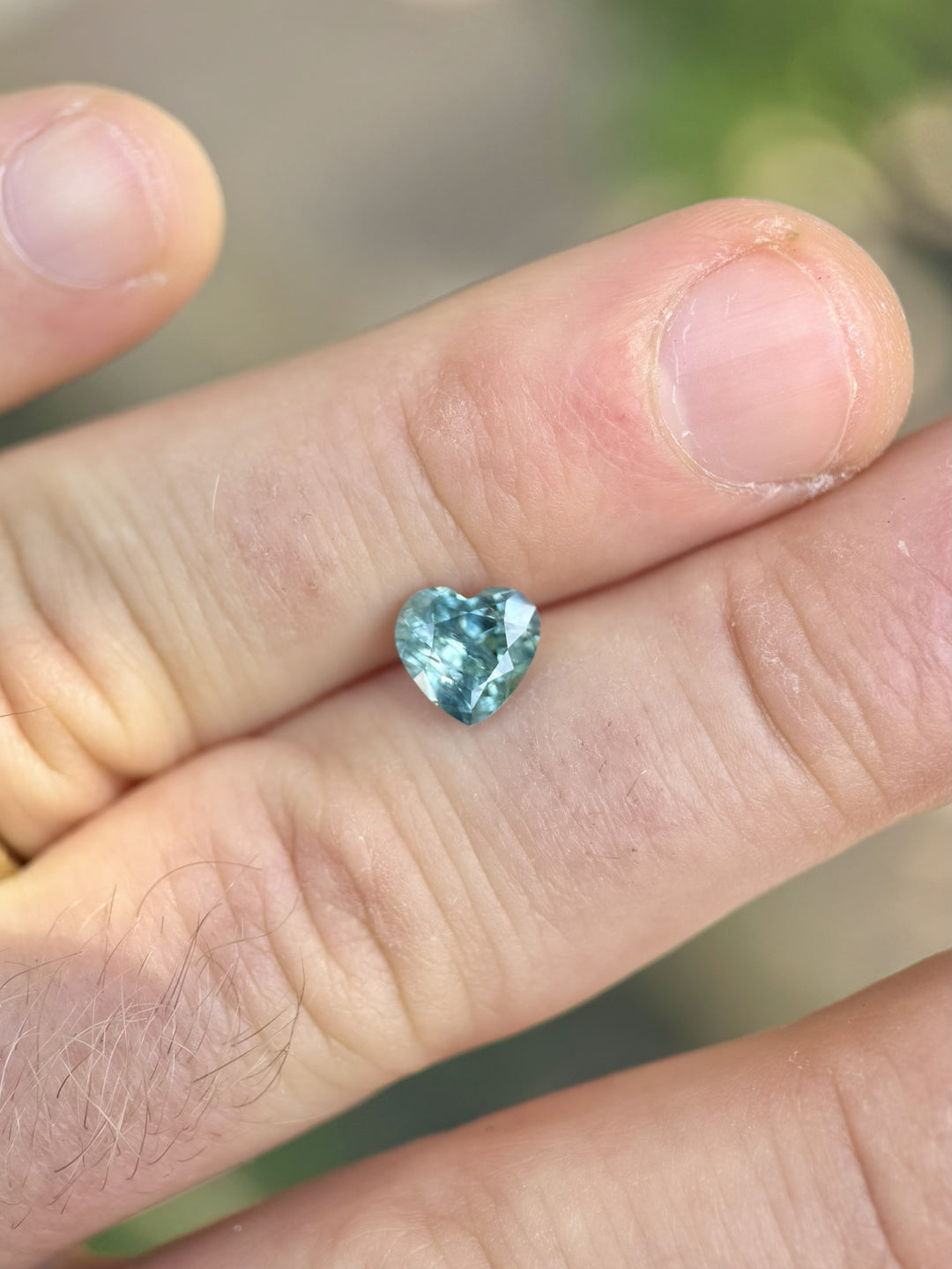 Montana sapphire in teal blue and green hues, heart cut, shown on fingertips – 1.71 carats.