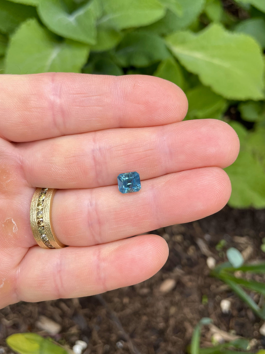 Close-up of a 2.50-carat teal, blue, and green sapphire in an Asscher cut, resting on a hand, sourced from the El Dorado Bar Deposit in Montana.