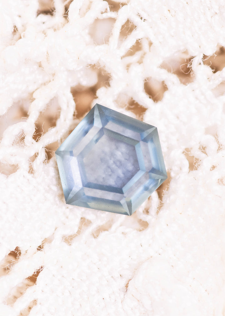 Teal blue seafoam sapphire photographed face-up on white textured fabric, showcasing a 1.37 carat geometric hexagonal step cut sapphire from Montana with crisp facets, untreated natural color, and clean symmetry.