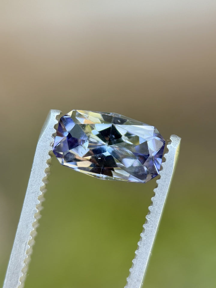 Elongated cushion Tanzanite in tweezers, 1.84 carats, with vivid purple, teal, and violet hues from Merelani Hills, Tanzania.
