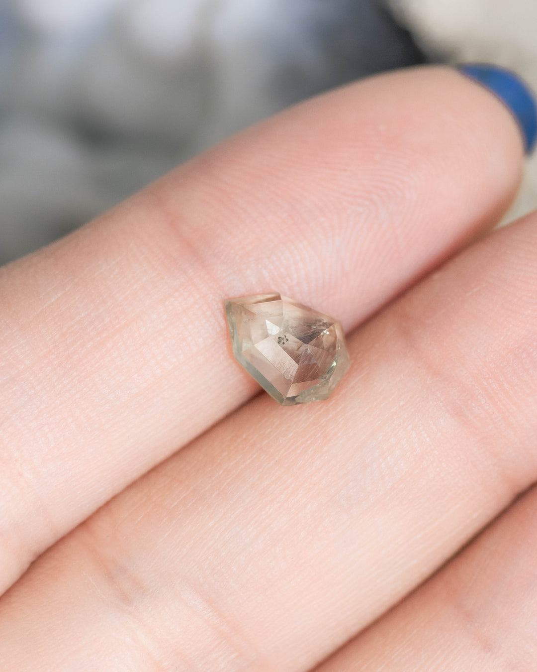 1.82 carat Montana sapphire resting on fingertip, teal and seafoam gradient shield rose cut gemstone, untreated USA origin sapphire showing faceted crown detail.