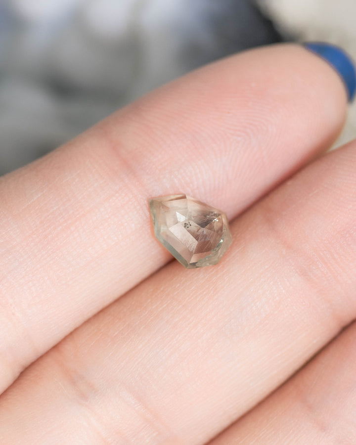 1.82 carat Montana sapphire resting on fingertip, teal and seafoam gradient shield rose cut gemstone, untreated USA origin sapphire showing faceted crown detail.