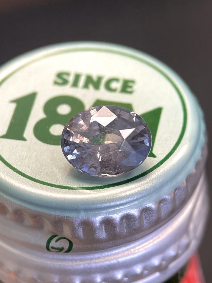 3.19-carat color change sapphire in an oval mix brilliant cut, resting on a green and white bottle cap, sourced from Sri Lanka.