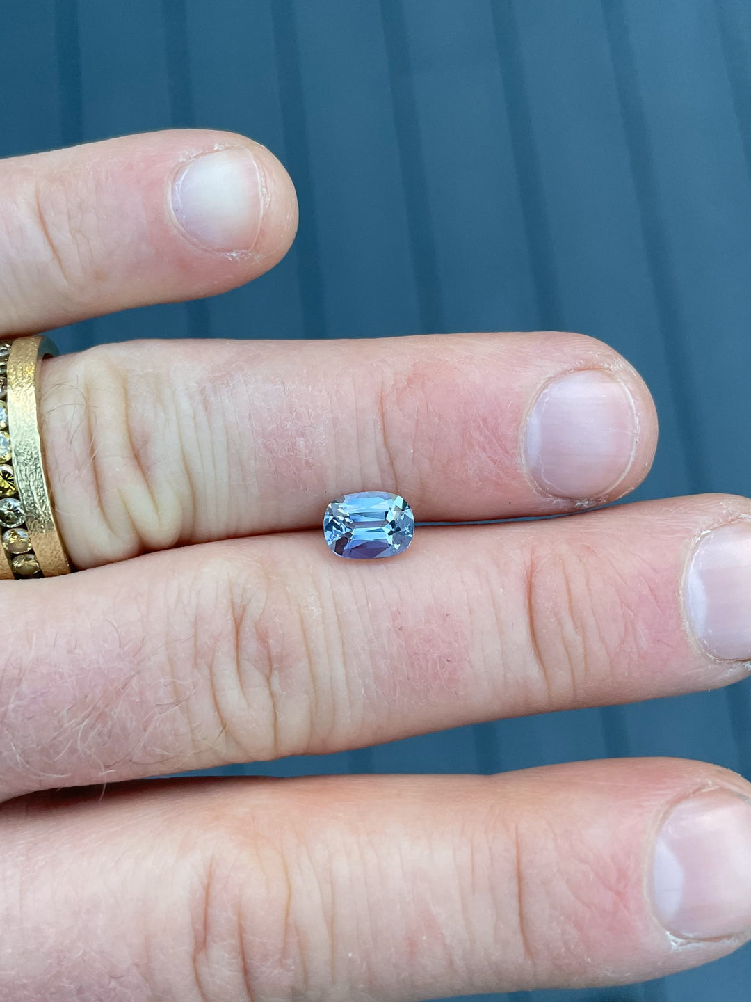 A 1.36-carat Tanzanite gemstone resting on fingers, revealing its deep teal-to-violet color shift in natural lighting.