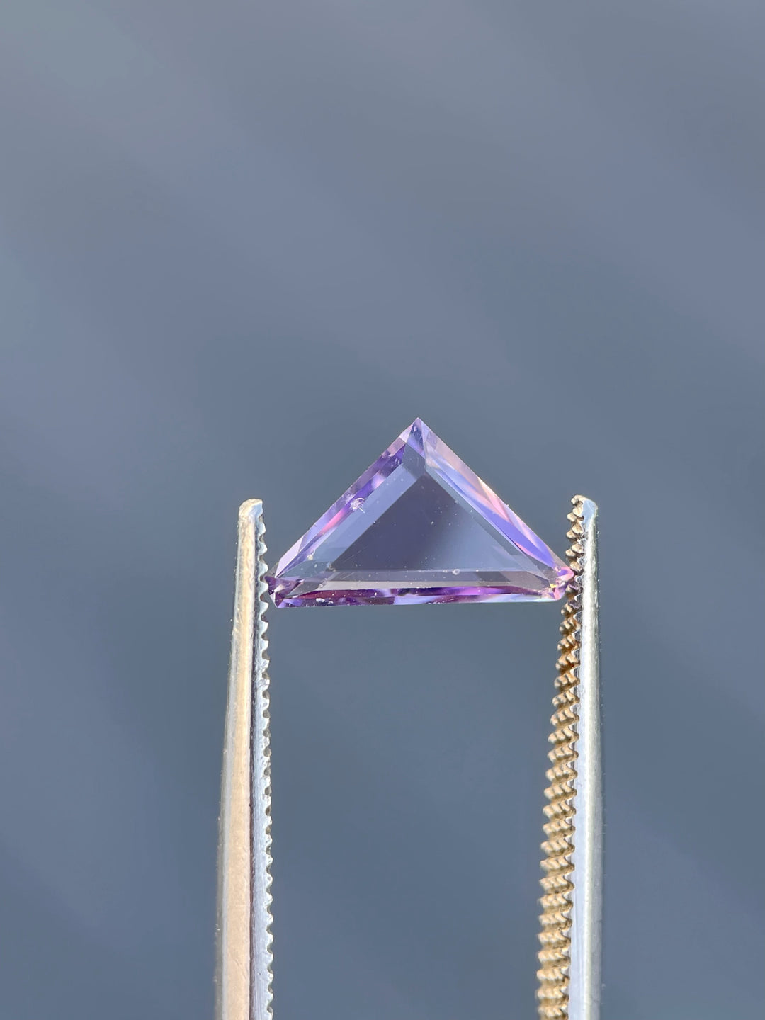 A delicate pink Spinel, 1.02 carats, cut in a trillion portrait style, highlighted against a gray background.