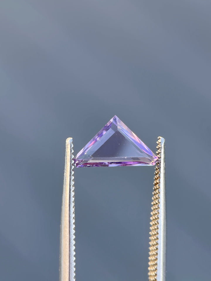 A delicate pink Spinel, 1.02 carats, cut in a trillion portrait style, highlighted against a gray background.