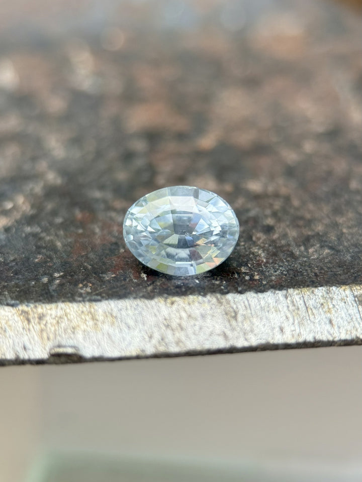 1.00ct Montana sapphire in teal and cornflower hues resting on fingertip, oval mix cut