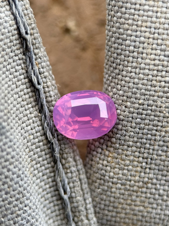 Close-up of a 1.53ct untreated sapphire resting on a woven fabric, exhibiting its vivid pink-purple tones and brilliant oval cut.