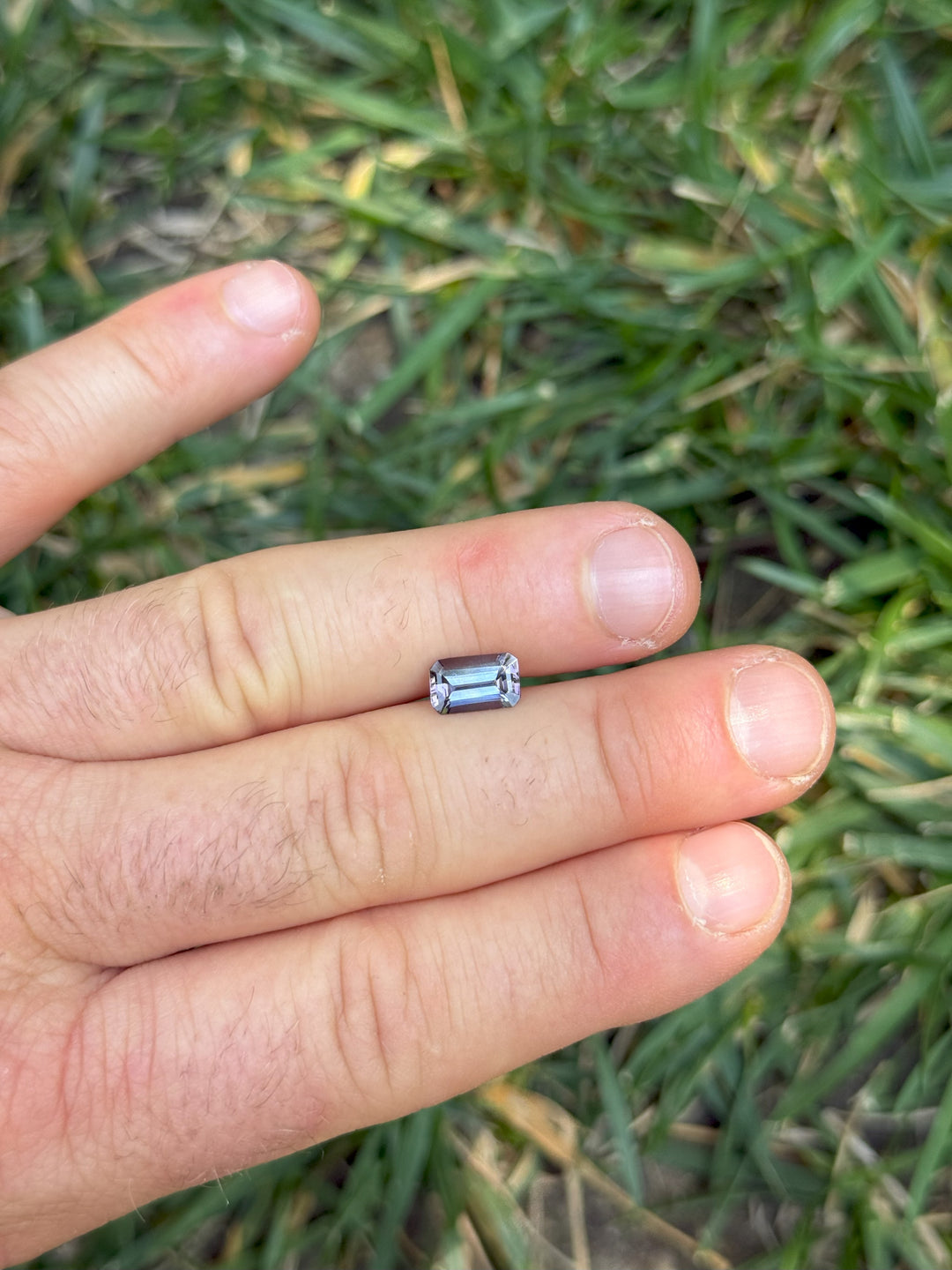 1.73-carat Tanzanite shown on fingers outdoors, highlighting its elongated emerald shape and color blend