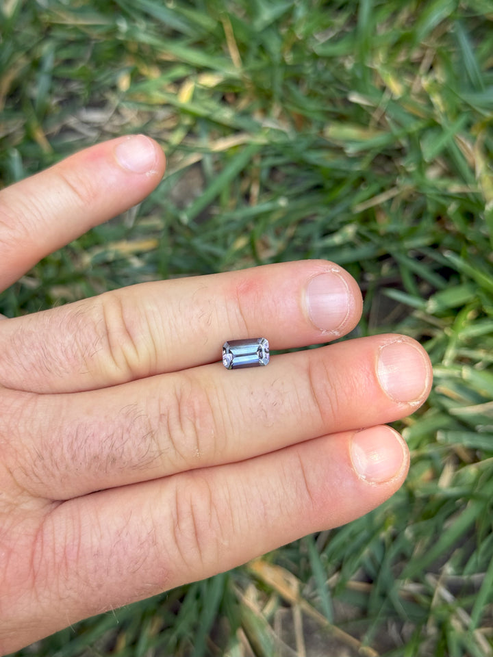 1.73-carat Tanzanite shown on fingers outdoors, highlighting its elongated emerald shape and color blend