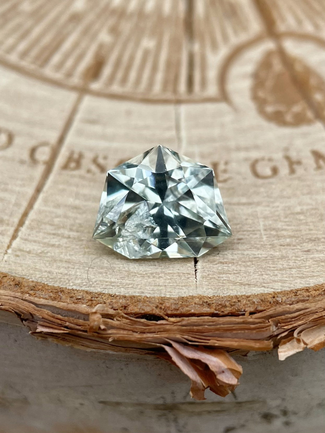 Natural trillion brilliant cut sapphire with a blue-green and yellow color mix, resting on wood, weighing 1.80 carats, unheated from Malawi.