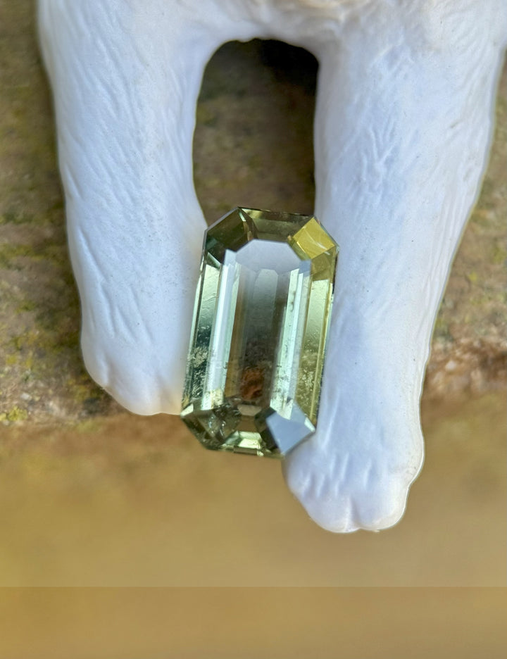 Close-up of unheated teal green sapphire from Tanzania in antique-style emerald cut resting on a white ceramic background